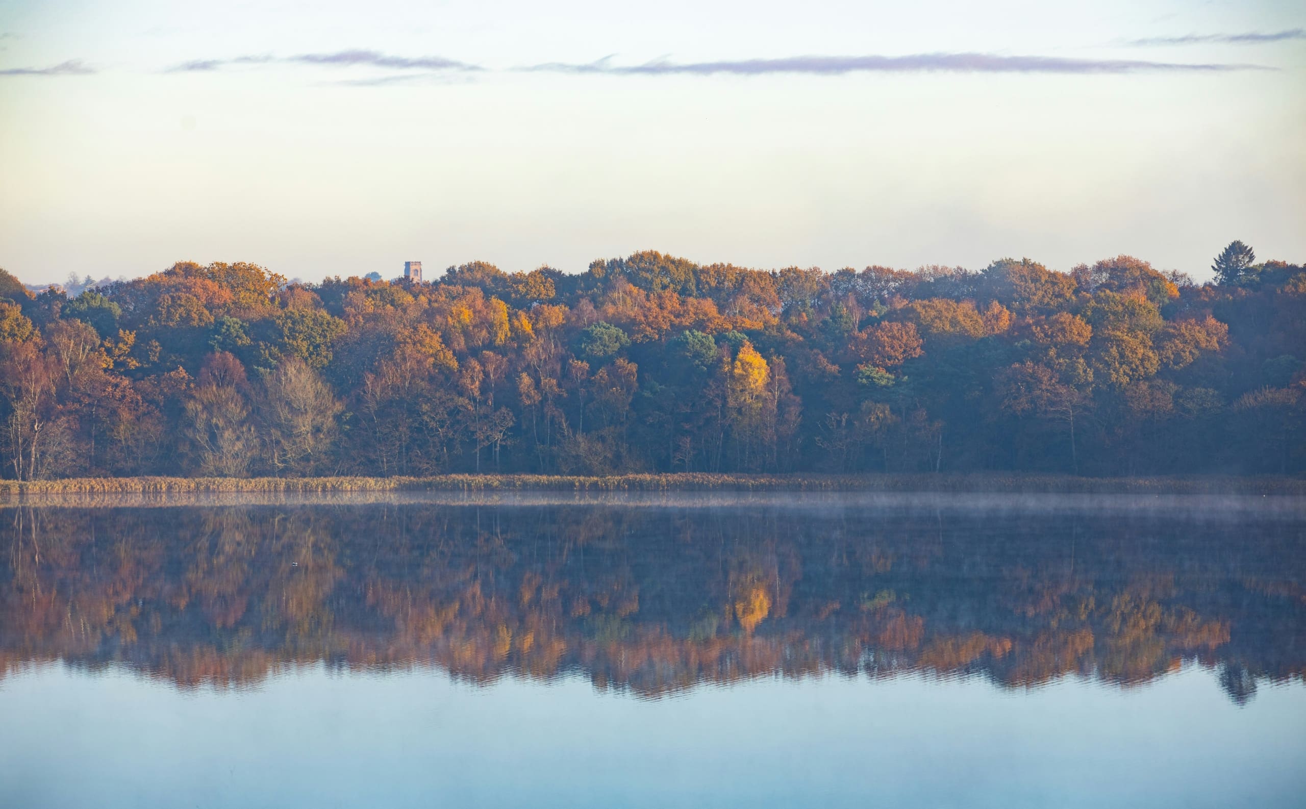 A Cheshire landscape of a calm lake reflecting autumn trees